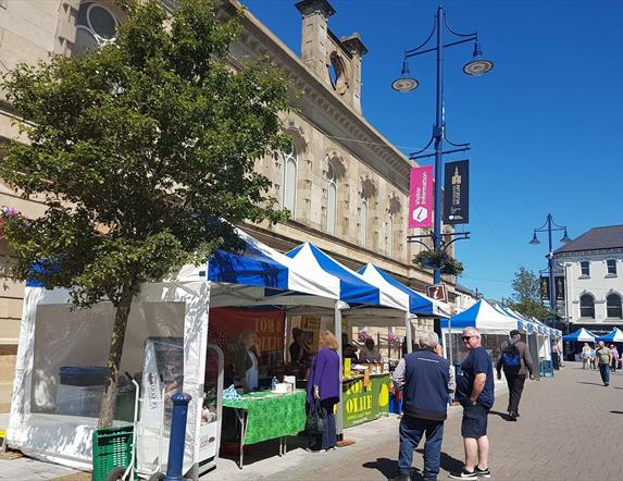 people browsing outdoor market stall tents on a sunny day