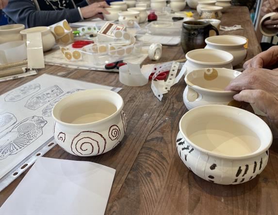 peoples' hands are painting small round pots