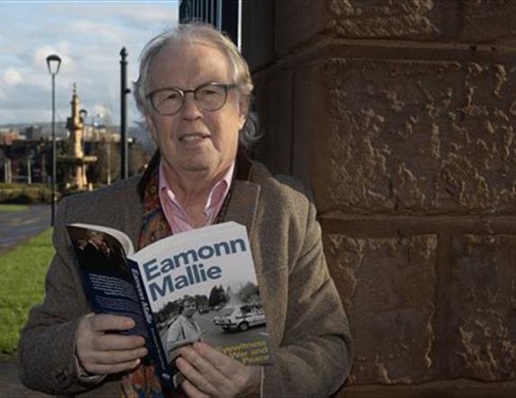 Eamonn Mallie stands holding his book