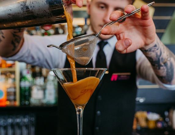 Bartender pouring a cocktail through a strainer into a martini glass at Elephant Rock Hotel