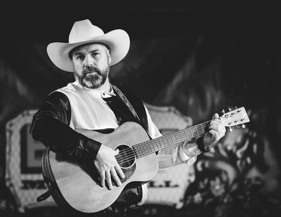Black and white photograph o Stephen Butler with a guitar in a cowboy hat.