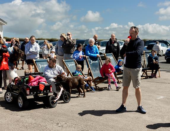 A family lounges on deck chairs surrounded by other families all taking pictures together and enjoying a day out, with a blue sky in the background.