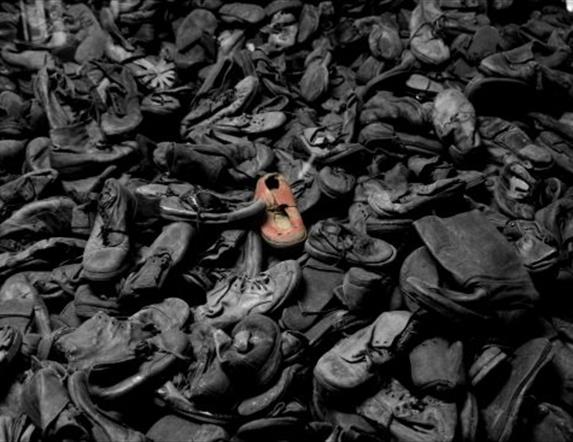 a large pile of abandoned shoes in black and white, except for one which is red