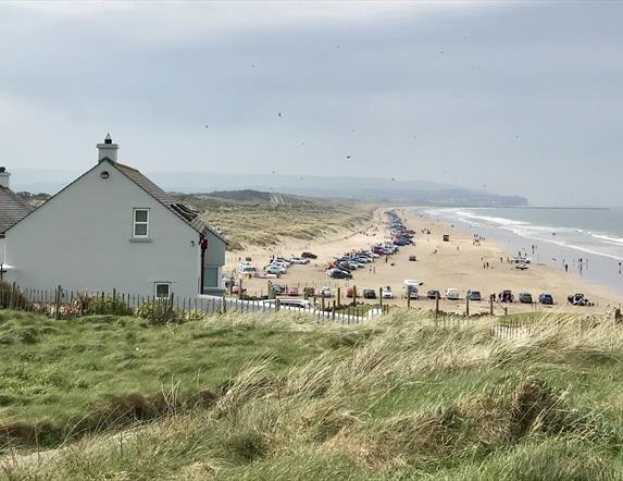 A view over Portstewart Strand in the busy summer season with cars parked all along the beach and families enjoying their day out.