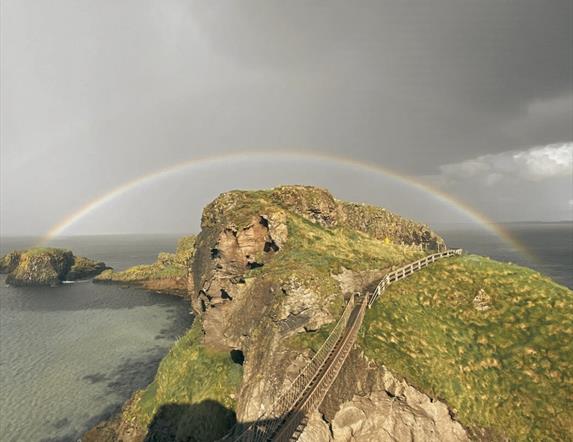 Picture of Carrick-a-Rede Rope Bridge with dark, moody grey skies and a rainbow