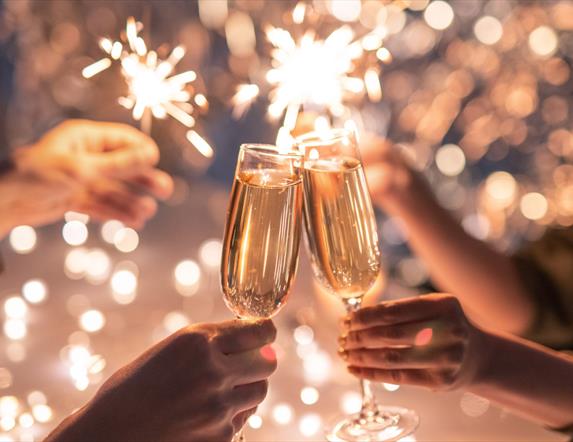 Wine glasses clink together in front of sparklers on New Year's Eve