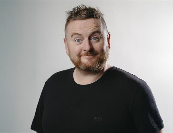 Paddy McDonnell smiles for the camera against a grey background with bright light.