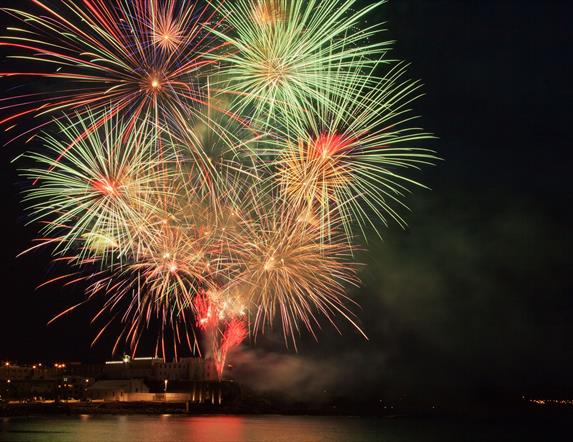 Fireworks burst to life above the sea and rocks, with the college in the background