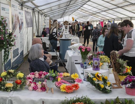 Crowds in a marquee looking at floral arrangements on a table covered with a white tablecloth