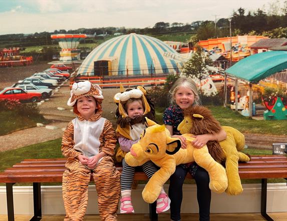 Three smiling children sitting on a bench, with two in animal costumes.