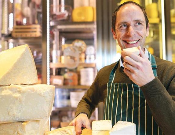 Kevin Sheridan in a striped apron, smiles while tasting cheese