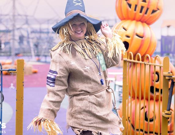 a person dressed as a scarecrow poses at Blair's Holiday Park, surrounded by pumpkin decorations