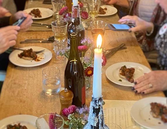 people are eating at a large wooden table by candlelight