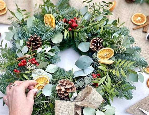 person's hand adds dried oranges to a festive christmas wreath