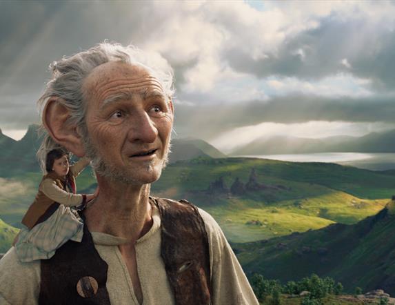 The BFG stands with a small child on his shoulder, with the countryside in the background.