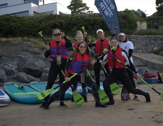 a group of people posing with paddles on a beach with paddleboard in the background