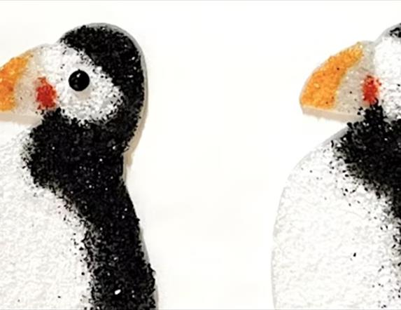 Two glass puffins facing left. They are flat against a white background.
