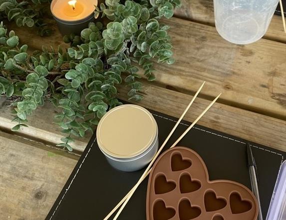 a wax melt mould sits on a wooden table, with a candle burning and other tools for making candles