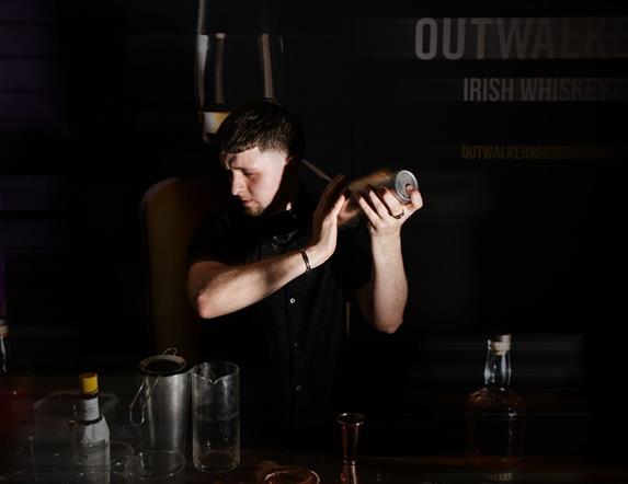 Man holding a cocktail shaker in a dimly lit bar setting