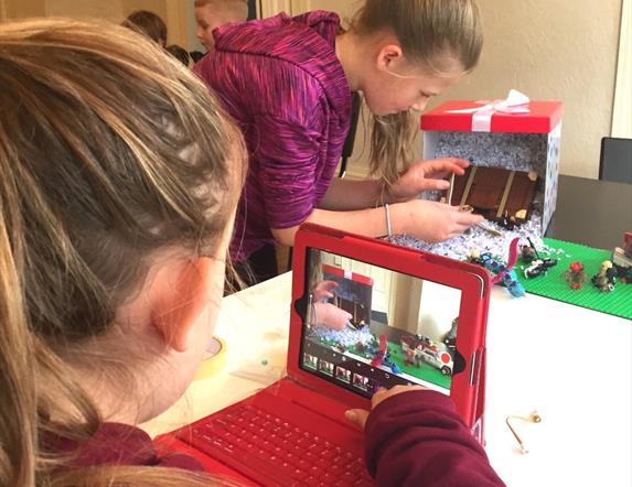 Children taking pictures of a small set using lego figures, to be animated in stop motion.