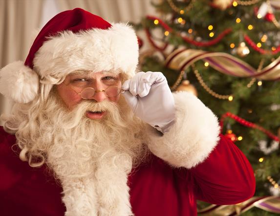 Santa peering over the rim of his glasses with a christmas tree in the background