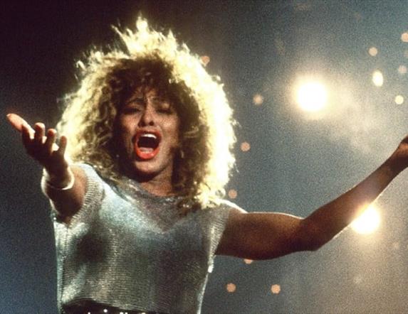 Tina Turner singing against sparkling lights with arms outstretched