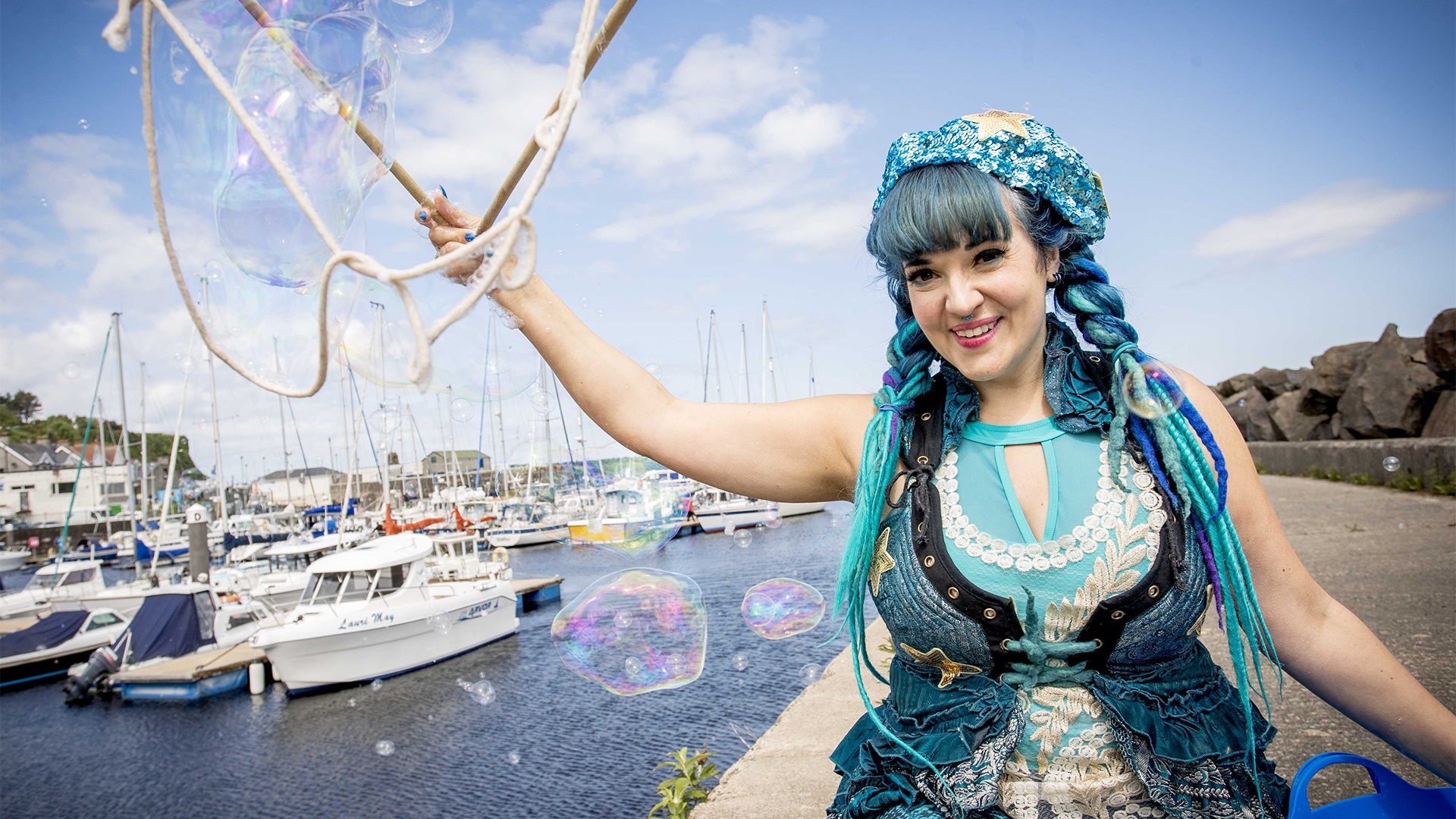 a woman dressed as a mermaid sitting by a harbour
