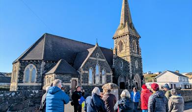 Bob Picken guiding a group dressed in outdoor clothing learning about the village of Castlerockclothing and hearing stories of the Earl Bishop