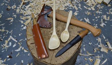 A photograph of wood-whittling tools and a carved spatula and spoon.