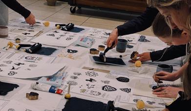 People gathered around a table, using rollers and stamps to create prints on paper. 