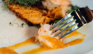 a plate of cooked fish, with a morsel on a fork covered in sauce