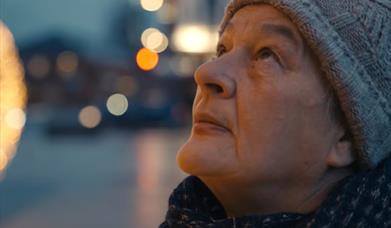 A woman wearing a hat, the city background is blurred.