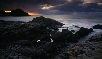 Image shows the Giant's Causeway as the sun sets in the distance