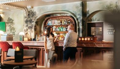 a man and woman clinking glasses while standing in front of the bar at the Leaping Hound Restaurant