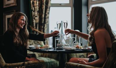 two women clink their prosecco glasses together over a table at Elephant Rock Hotel