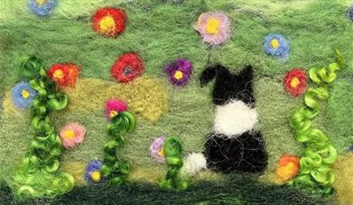 a felted piece with a dog in a field of flowers