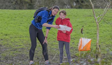a woman and a girl outdoors, reading from a map. the girl is pointing the way