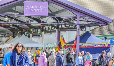 people walking through a market square with stalls