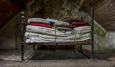 a bedframe with many mattresses stacked up on it in an empty attic