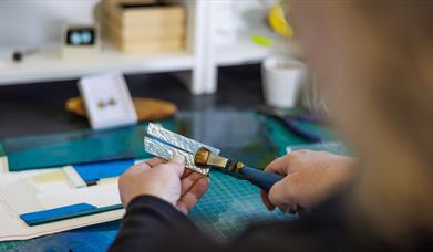 a glass artist uses a cutting tool as part of the fused glass-making workshop