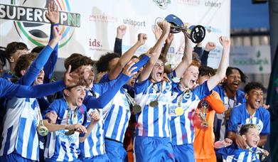 a male youth football team celebrates winning a trophy