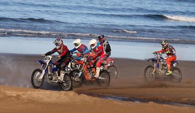 Riders on the sand with waves in the background