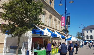 people browsing outdoor market stall tents on a sunny day