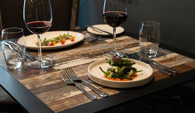 dishes of food and red wine sit on a wooden dining table