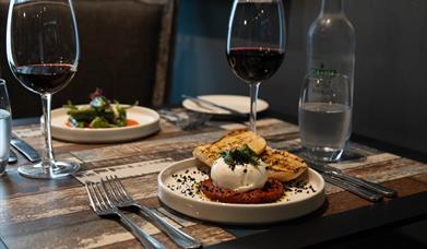 dishes of food and wine glasses sit on top of a wooden table