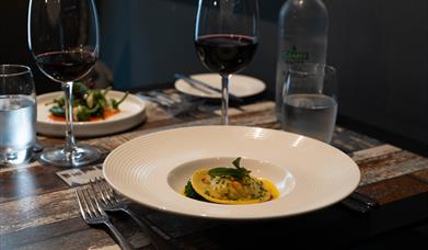 Italian food in dishes and red wine sit on a table in a restaurant