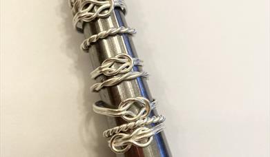 a selection of handmade silver rings in the shape of knots on a ring sizer.