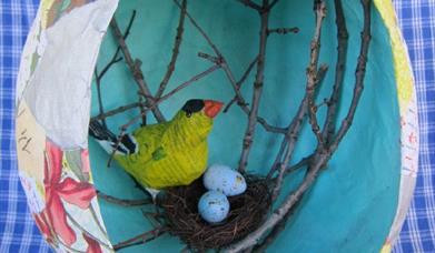 a paper-mache easter egg with a crafted bird and nest inside