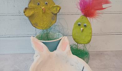 image of a handmade clay bowl in the shape of a bunny with clay chicks on sticks painted yellow in the background.