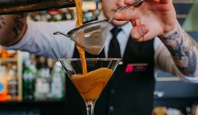 Bartender pouring a cocktail through a strainer into a martini glass at Elephant Rock Hotel